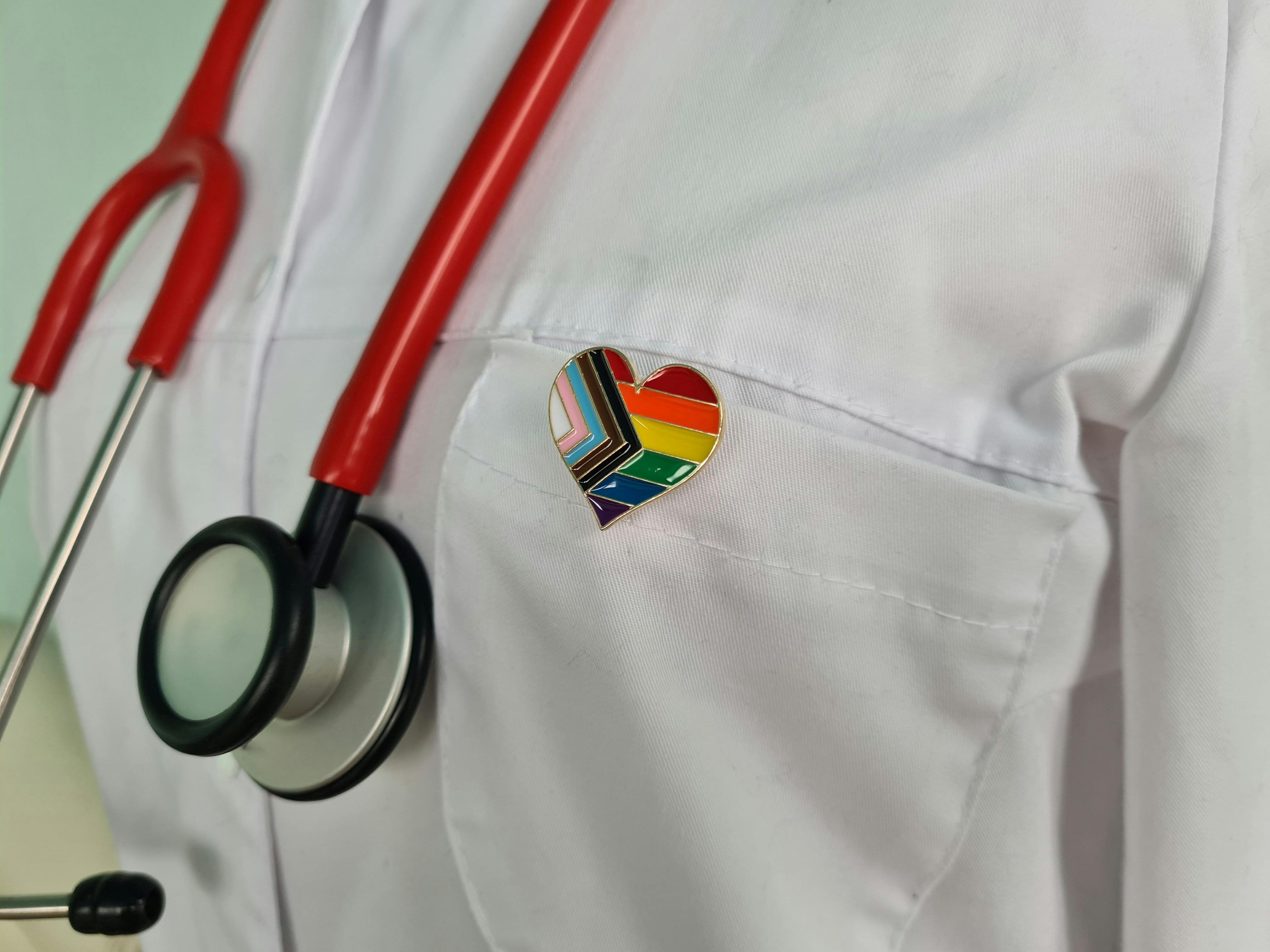 Silhouette of doctor in white coat with stethoscope and LGBT badge on pocket.